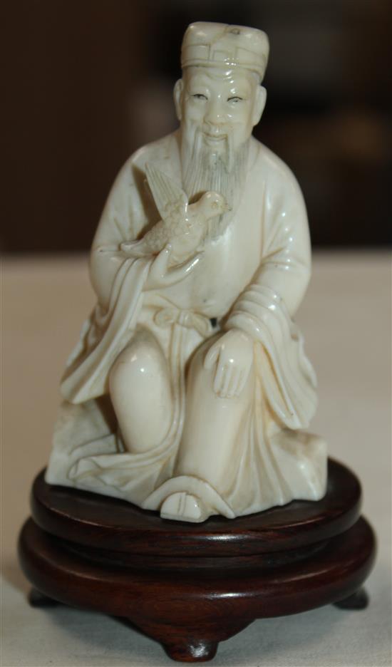 A Chinese ivory seated figure of a scholar holding a bird, early 20th century, wood stand, total height, 10cm